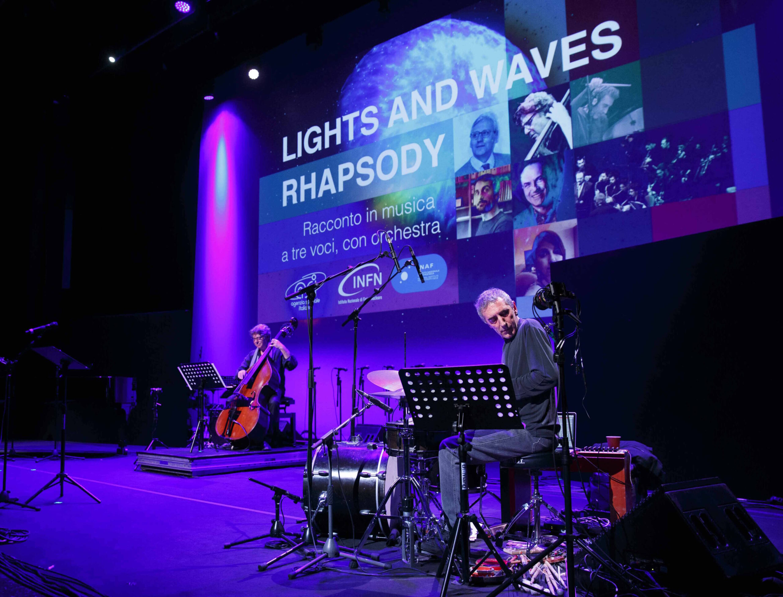 Musicisti con luce viola sul palco dello spettacolo Lights and Waves Rhapsody. Un percussionista e un contrabassista