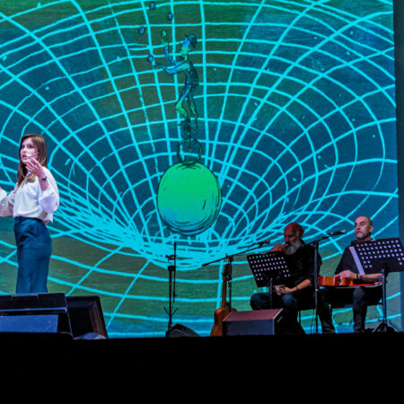 Valentina Mariani sul palco durante lo spettacolo l'Universo in un Battito d'Ali, come sfondo. un'illustrazione di Luca Ralli sullo spaziotempo