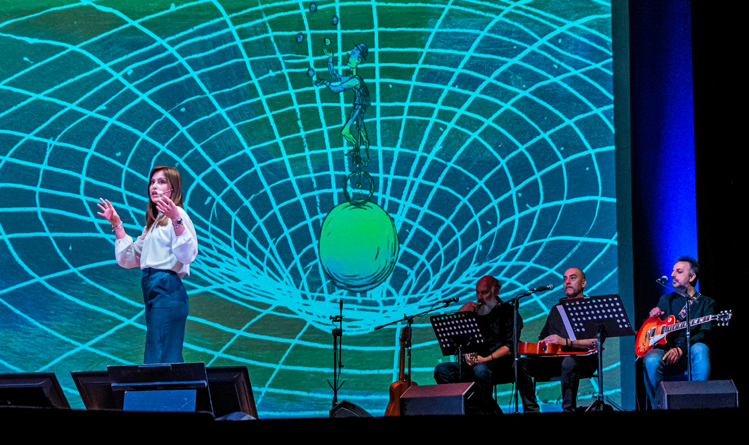 Valentina Mariani sul palco durante lo spettacolo l'Universo in un Battito d'Ali, come sfondo un'illustrazione di Luca Ralli sullo spaziotempo