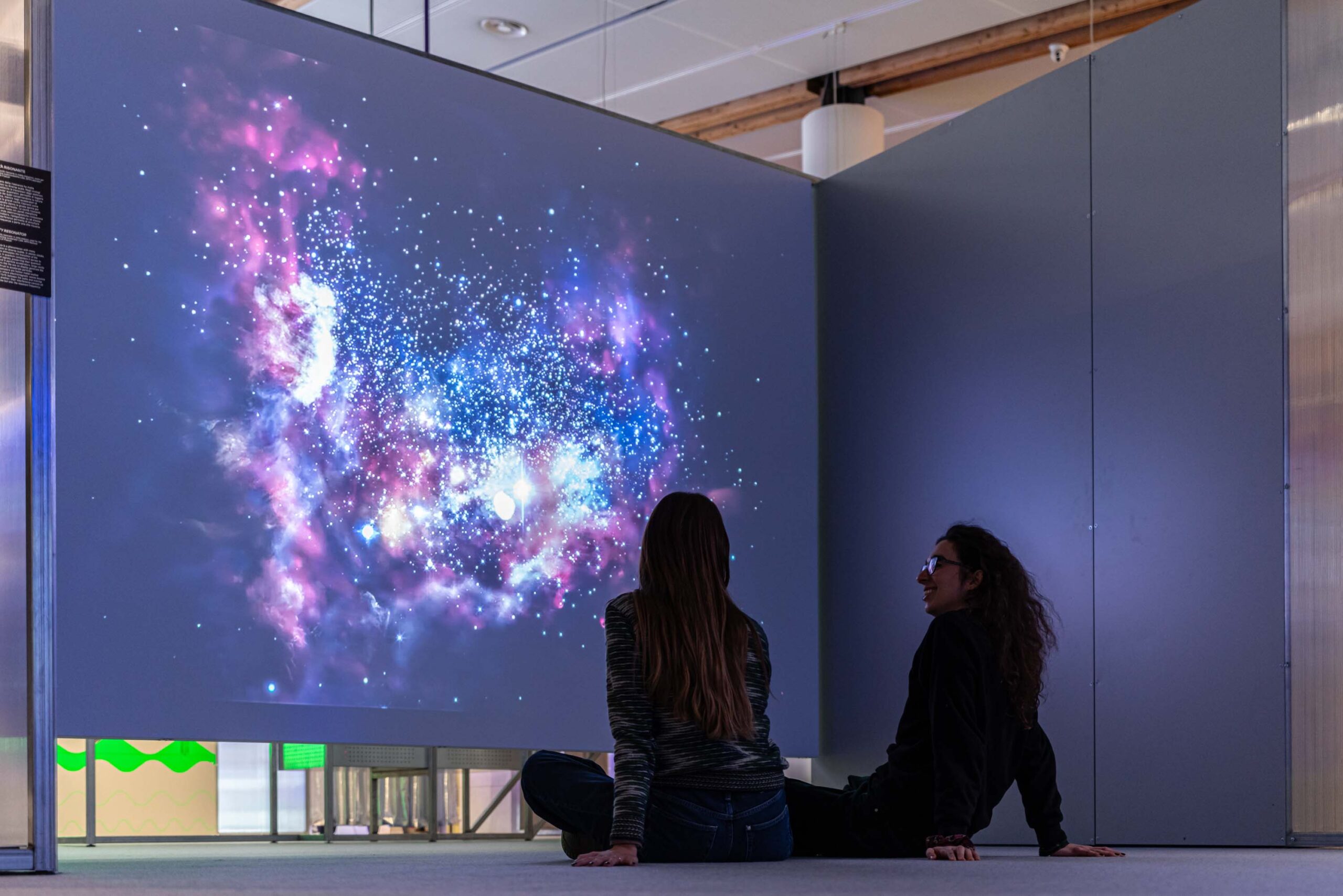 Due ragazze guardano la proiezione sul cosmo alla mostra Quanto